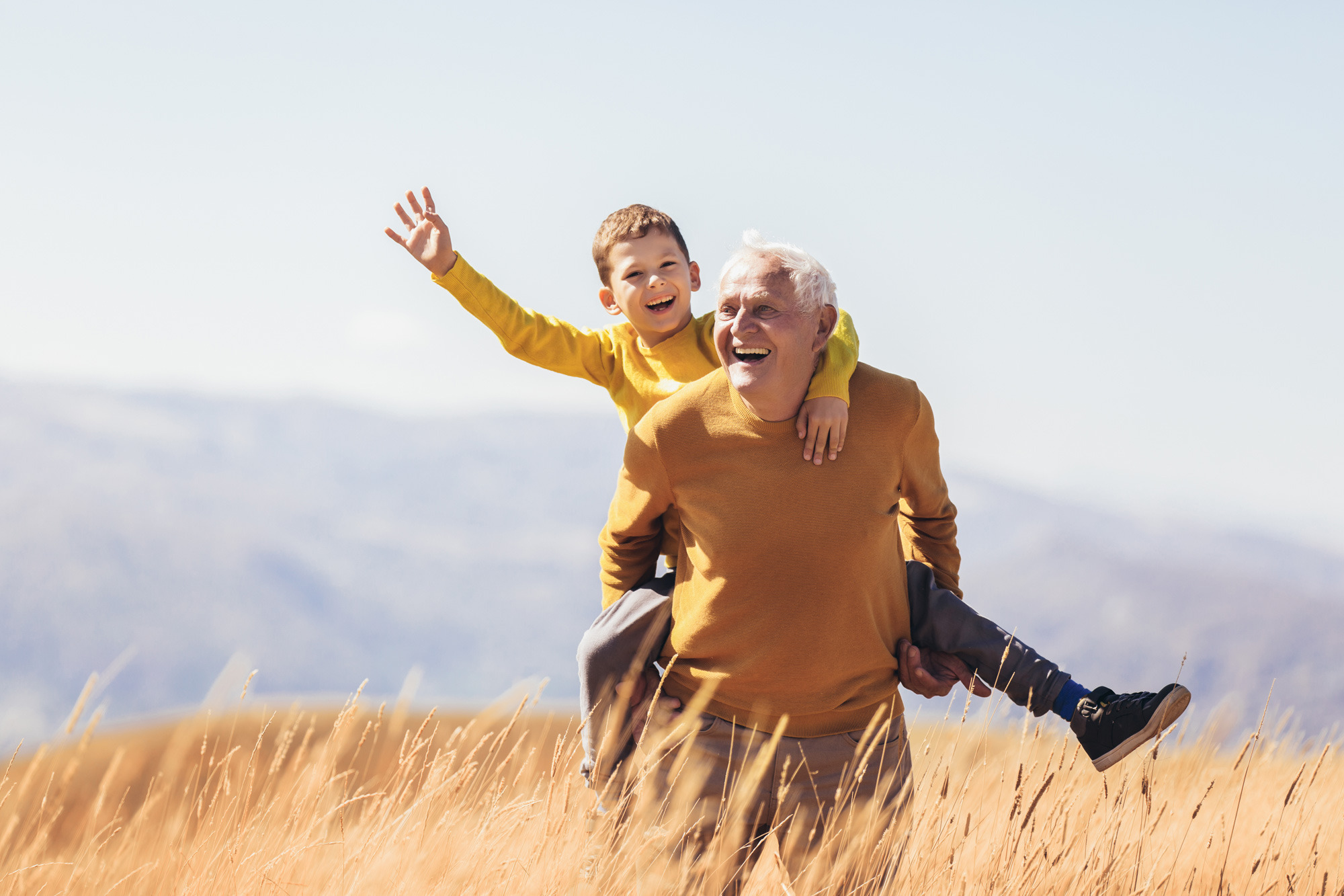 Grandfather giving a piggy back to his grandson in the long grass, both with huge grins. Aster Care's Dementia Care Policy takes into consideration the individuality of the person and recognises the need to involve the family members or key people in the cared-for person’s life,